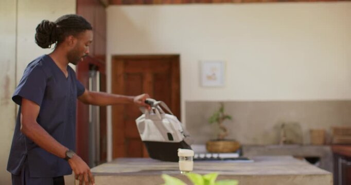 Man in scrubs entering kitchen with bag, placing folded item, checking phone pre-shift