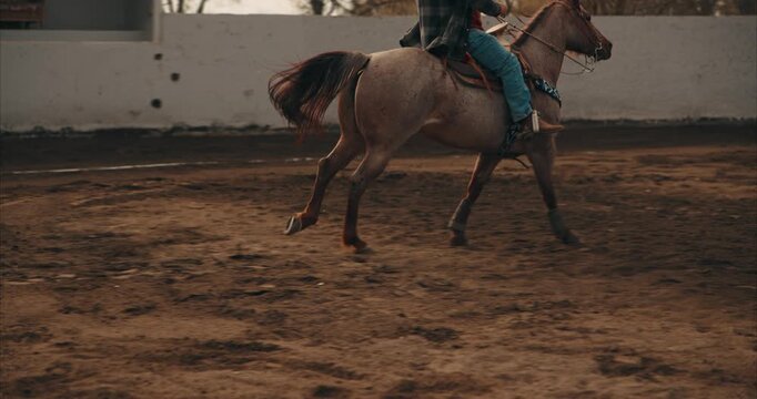Cinematic tracking shot of a rider on horseback galloping and kicking up dust in a dirt arena