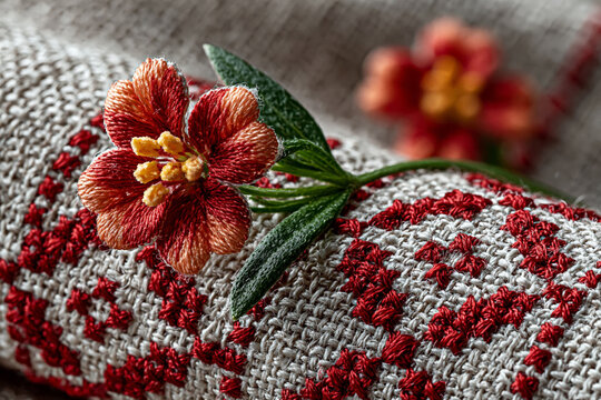 Macro shot of traditional Mari folk embroidery on a linen sleeve, featuring a 3D red flower with intricate needlework details and geometric ethnic patterns