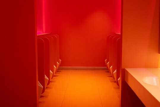 Red public bathroom with rows of urinals