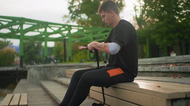 white man practicing walking pole therapy on bench steps by pond rehabilitation exercise focused on balance and posture guided routine tactile grip visible tattoos casual workout clothing late