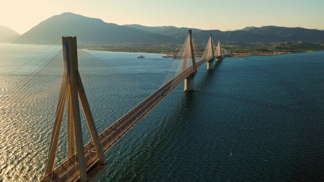 Golden hour sunlight reflecting on the sea during an aerial flight revealing the magnificent rio-antirrio bridge. A major engineering landmark connecting the peloponnese peninsula to mainland greece