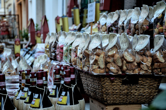 A traditional Italian market stall displaying straw‑wrapped wine bottles and bags of biscotti, arranged neatly in wicker baskets and illuminated by warm ambient light.
