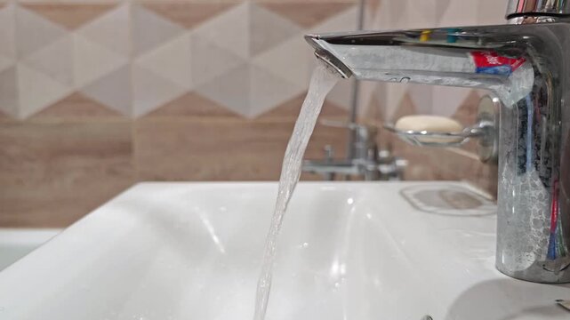 Water flows from a faucet while hands adjust the tap in a bathroom sink