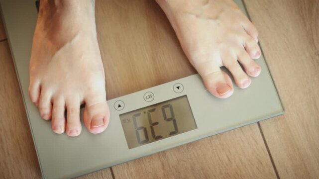 Close up person legs bare feet stepping onto weighing scale at home. Healthy lifestyle weight awareness concept. Woman weight lose standing on scales measure weight. Fitness diet BMI woman slimming.