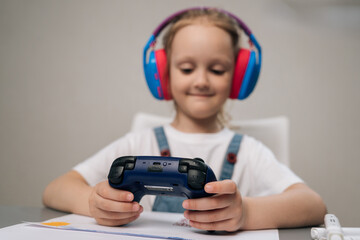 Portrait of young girl in colorful headphones plays video game, holding controller. Shallow depth of field focuses on gamepad in hands. Represents modern childhood, digital entertainment, leisure. © dikushin