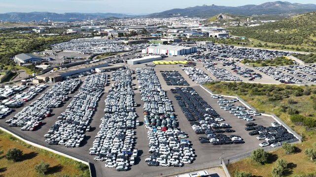 Thousands of brand new cars parked in a massive outdoor storage lot, awaiting distribution and export to dealerships, symbolizing the automotive industry's mass production and logistics
