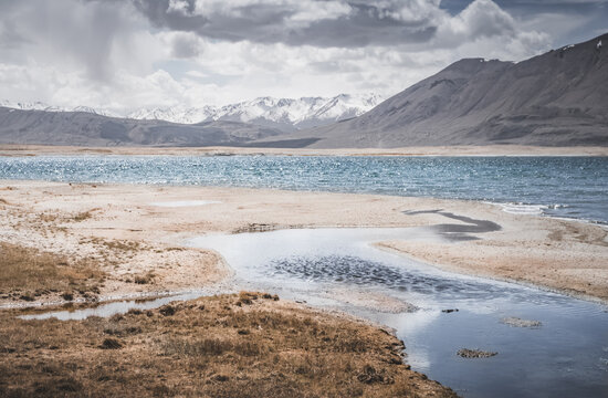 Mountain landscape, a cold high-altitude lake against the backdrop of rocky peaks and ridges with snow and glaciers, a panorama in the Tien Shan Mountains in the Pamirs, a lake with waves