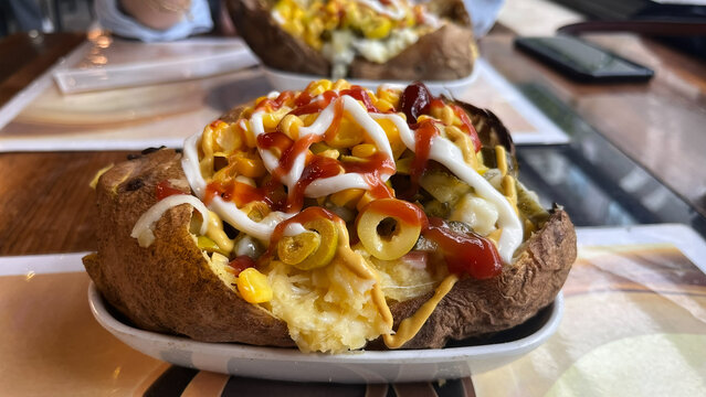 A generously stuffed baked potato; a traditional Turkish street food served with corn, olives, ketchup, and mayonnaise.
