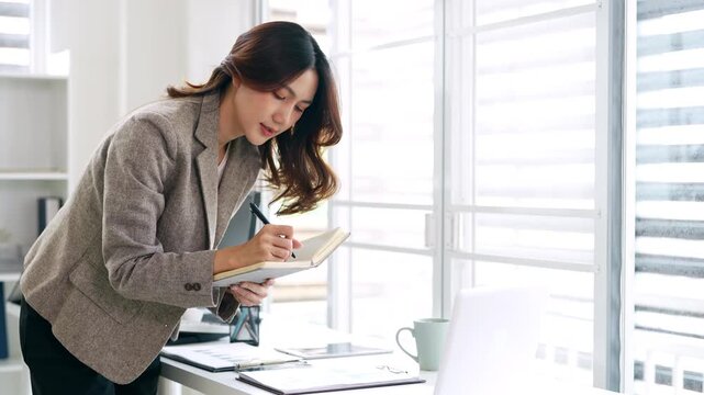 Young businesswoman hand holding pen taking notes , sitting at desk with laptop , analyzing information.