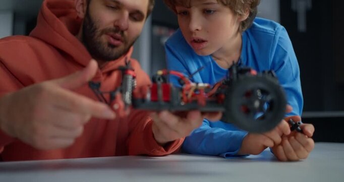 Father and young son repairing a remote control car together at a table, examining wheels, wires, and chassis during a hands-on home electronics project
