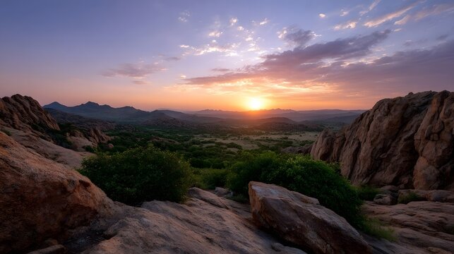 Sunrise illuminates rugged rock formations overlooking a vast green scrubland valley under a pastel sky