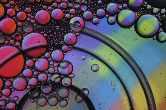 Gotas de agua sobre CD con luz multicolor, crea un fascinante efecto iridiscente con colores arco&iacute;ris. Las burbujas act&uacute;an como lentes naturales, generando patrones circulares y reflejos vibrantes.
