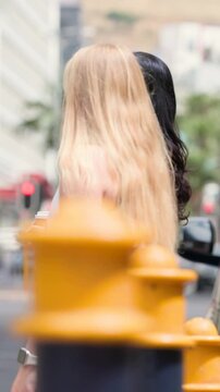 Vertical video: Holding coffee woman standing curb as blonde joining man crossing near hydrant