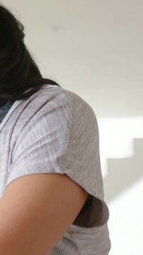 Vertical video: Camera pulling back woman turning torso at home showing gray top bra strap hair tie
