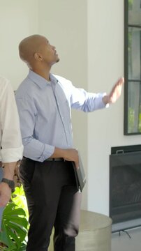 Vertical video: Entering man in blue shirt holding folio, guiding client through modern living area