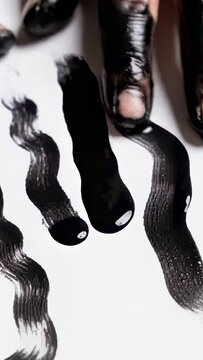 Vertical video: Lowering painted tips touching white sheet on table, dragging to form black strokes
