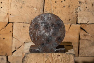 Close-up of a used round steel shooting target on a wooden block stand with fresh and old bullet marks after range practice © Dmitri