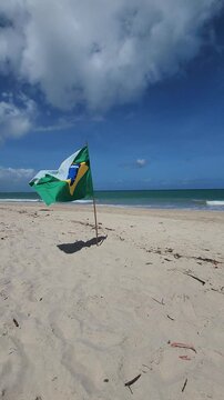 Vertical video of the flag of Brazil on a beach with turquoise water in the State of Pernambuco.