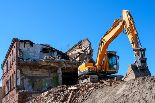 Excavator demolishing old brick building amid rubble on urban construction demolition site scene