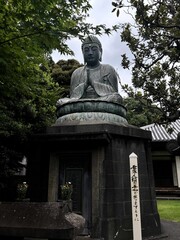 Obraz premium Bronze Buddha statue in a traditional Japanese temple garden, surrounded by lush green trees. A serene and sacred religious monument representing Buddhist culture and spirituality in Japan.