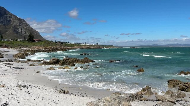 Hermanus coastline in South Africa with ocean waves, sandy beach and deep blue sky, beautiful summer landscape with relaxed holiday atmosphere.