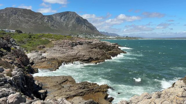 Hermanus coastline in South Africa with ocean waves, sandy beach and deep blue sky, beautiful summer landscape with relaxed holiday atmosphere.