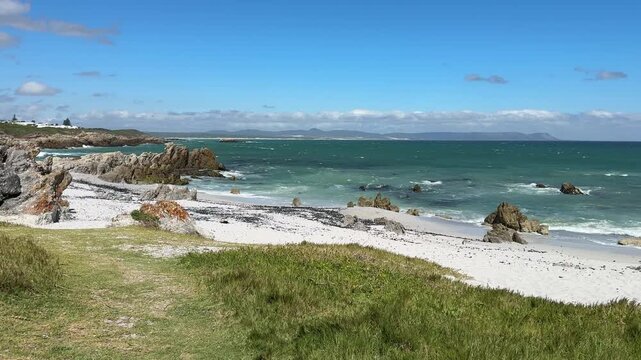 Hermanus coastline in South Africa with ocean waves, sandy beach and deep blue sky, beautiful summer landscape with relaxed holiday atmosphere.