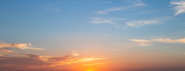 Panoramic sunset sky background with vibrant orange and golden clouds under a soft blue twilight sky © Choat