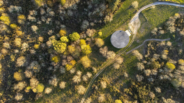 Aerial view of a circular concrete structure nestled among colorful autumn trees and winding dirt paths in a rural landscape Taboadela, Ourense, Spain.