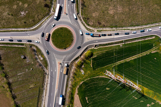 Aerial view of traffic moving through a circular roundabout surrounded by green fields and an electricity pylon in Brasov, Brasov, Romania.