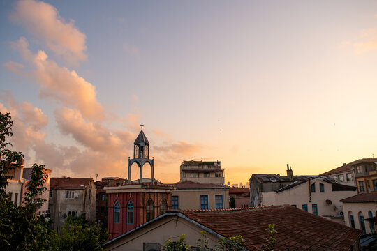 Golden sunset over the rooftops of a historic Istanbul neighborhood, featuring a small church bell tower and a soft, cloudy sky.
