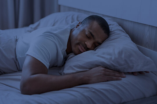 African american man sleeping at night in bedroom with blue light tone. Healthy lifestyle concept of deep sleep, rest and circadian rhythm, closeup