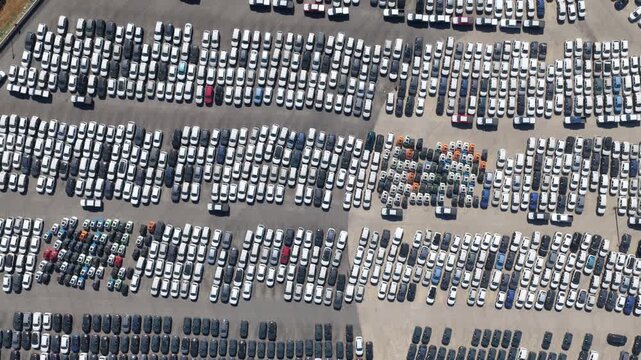 High-angle drone perspective revealing thousands of new cars neatly arranged in a massive parking lot, showcasing the scale of automotive manufacturing, export, and global distribution