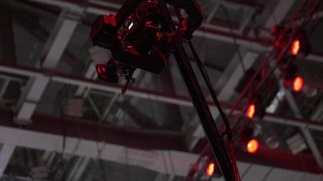 Red stage lights illuminate camera rig and truss, creating dramatic concert atmosphere and industrial mood.