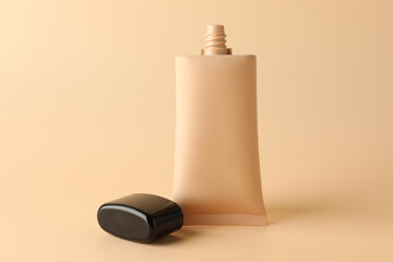 Naklejka premium Skin foundation in tube and lid on beige background, closeup