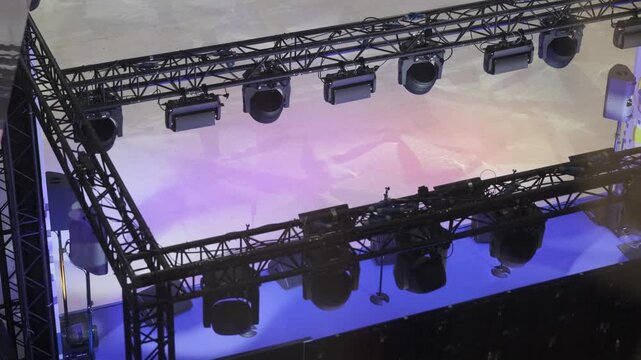 Overhead stage lighting and metal truss rigging casting blue and purple wash on empty performance area, professional concert production setup, technical gear and stage atmosphere.
