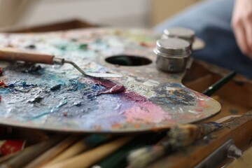 Fototapeta premium Woman with paints, palette, brushes and knife indoors, closeup