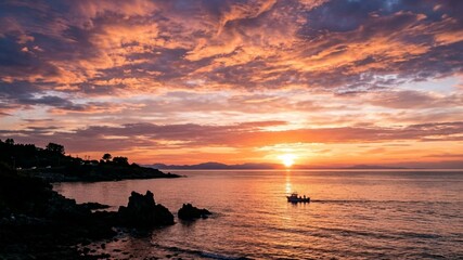 Naklejka premium Beautiful Sunset Over the Ocean with a Small Fishing Boat and Dramatic Orange Clouds