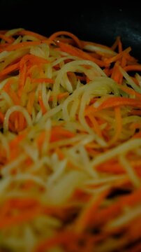 Chopped vegetables, carrot, daikon mooli, bell pepper, tomatoes, garlic frying in olive oil on a pan, close up. Сast iron skillet, Food in motion, process . Cooking, restaurant cookery