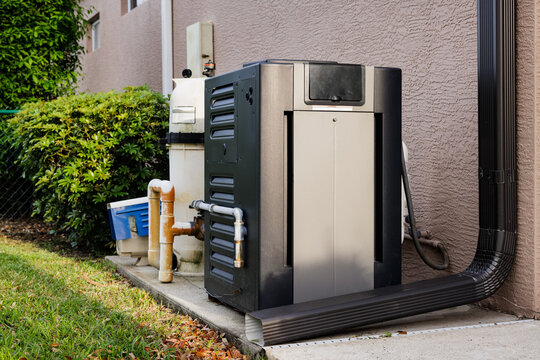 Modern natural gas swimming pool heater unit and pool water filtration equipment on concrete slab outside of house.