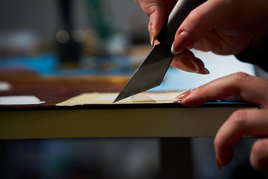Hands of an artisan cutting raw leather around a paper template with a knife.