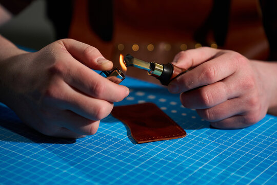 Artisan using a lighter to heat an edge creaser over a blue cutting mat in a workshop.
