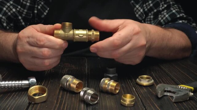 Hands assembling brass plumbing fittings with various connectors and tools on a wooden work surface in a well-lit workshop environment