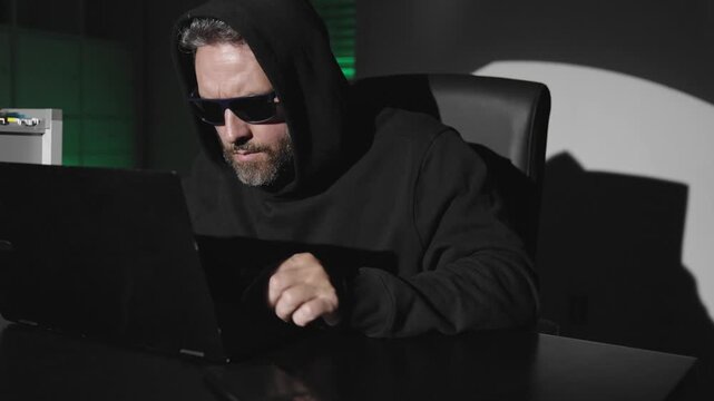 Laptop hacker involved in cyber espionage. Hooded hacker targets blockchain technology. Cyber hacker breach exposes private data. Anonymous hacker operates on dark web.