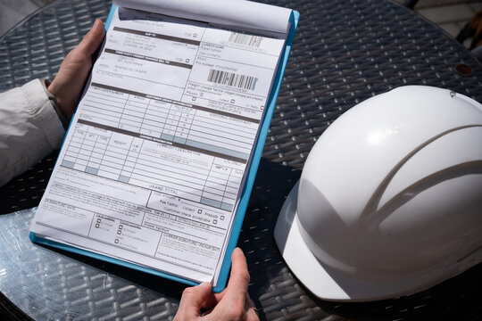 The worker holds a tablet with documents or bill of lading a protective helmet.
