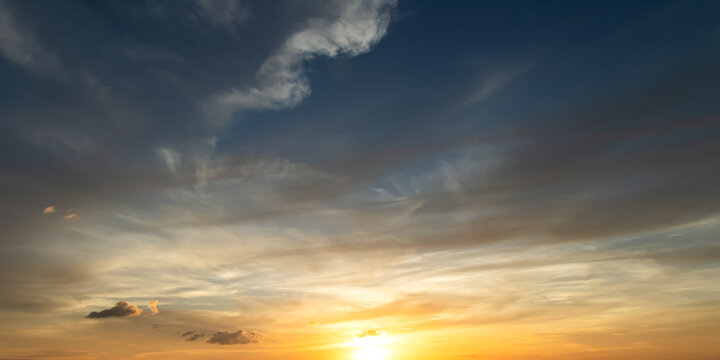 Beautiful sunset sky with golden light and wispy cirrus clouds over dark blue twilight background for nature wallpaper