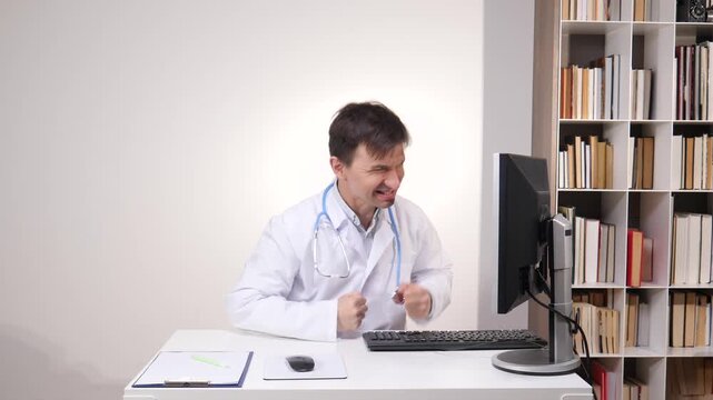 Male doctor experiencing burnout and stress, looking angrily at a computer screen while working at his desk in a medical office, depicting frustration with technology and workload