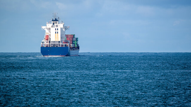View of a large container ship carrying colorful cargo across the calm blue waters of the Atlantic Ocean under a cloudy sky Lisbon, Lisbon, Portugal.