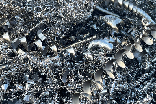 Curled metal shavings fill the frame with shiny silver texture. Sharp industrial scrap creates abstract pattern. Recycling and machining detail forms strong metallic background for industry design.
